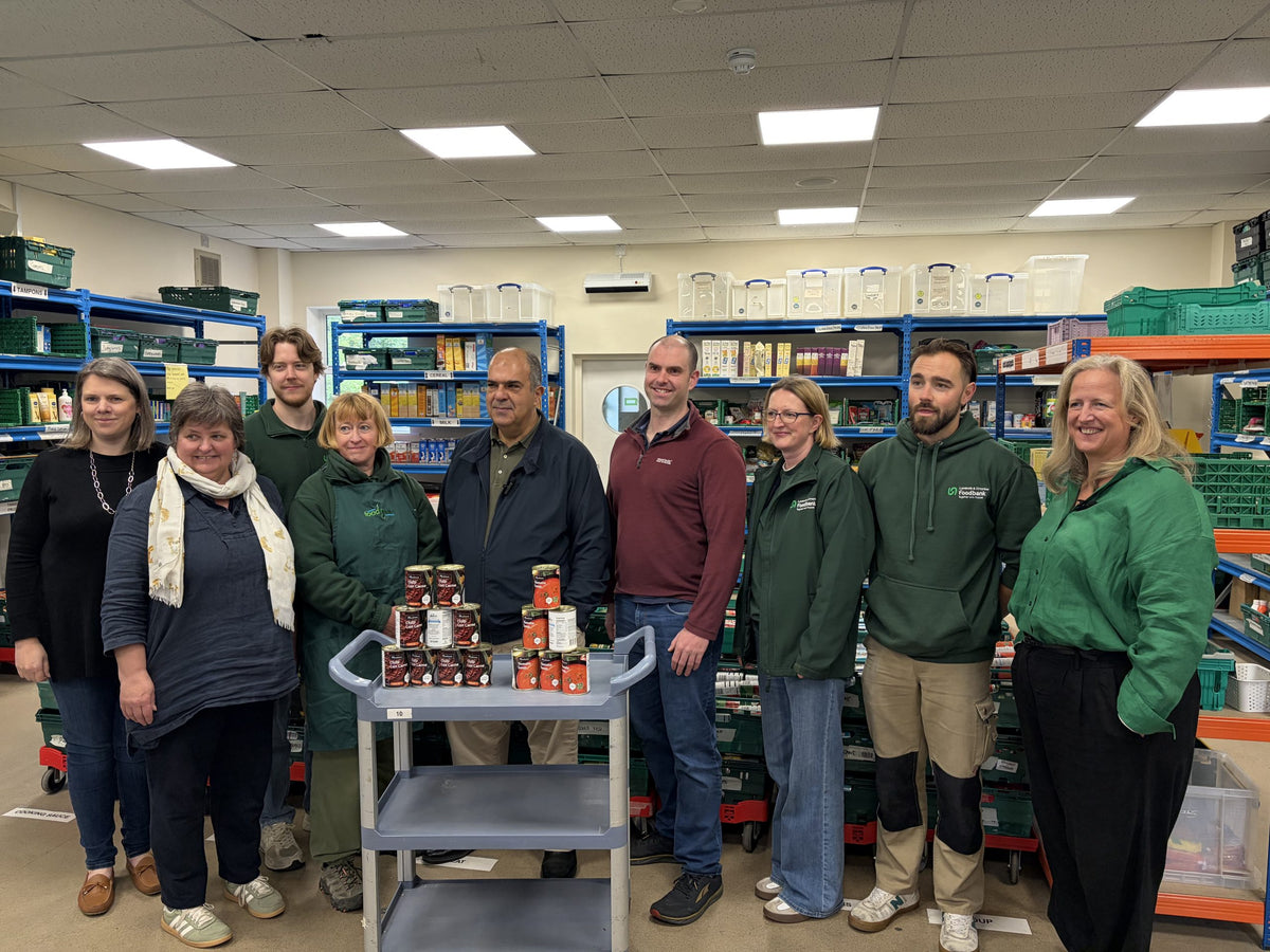 Sir Stelios with staff and volunteers at a UK food bank, beside donated canned food.